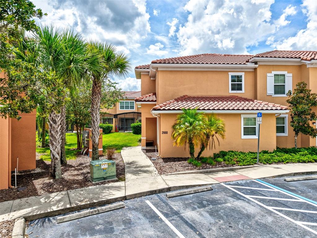 A two-story tan stucco townhouse with a tile roof and a concrete walkway — 2668 CORVETTE LANE, KISSIMMEE, FL