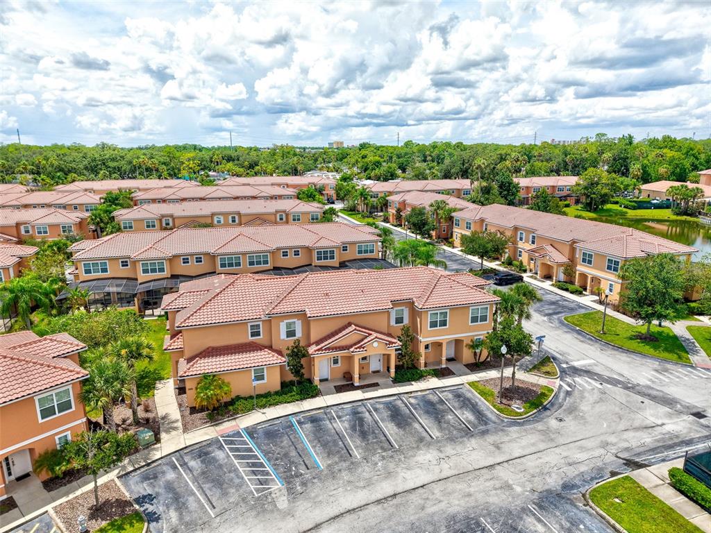 An aerial view shows multi-story tan apartment buildings with red tile roofs and parking lots — 2668 CORVETTE LANE, KISSIMMEE, FL