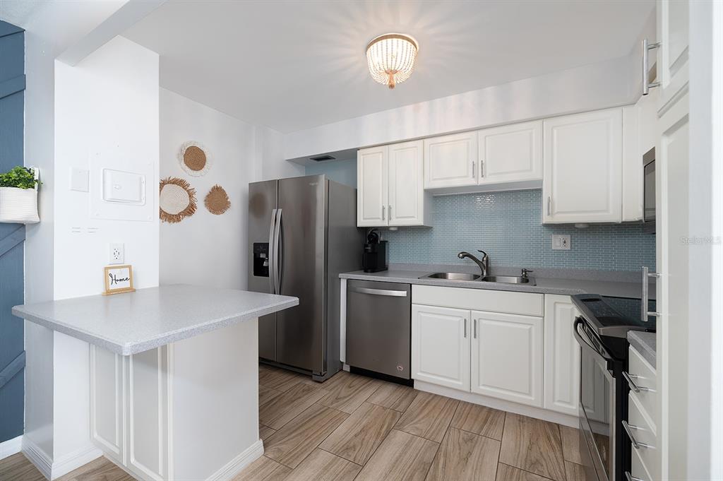 A kitchen features white cabinets, stainless steel appliances, a light blue backsplash, and wood-look flooring — 2800 N ATLANTIC AVENUE UNIT 1401, DAYTONA BEACH, FL