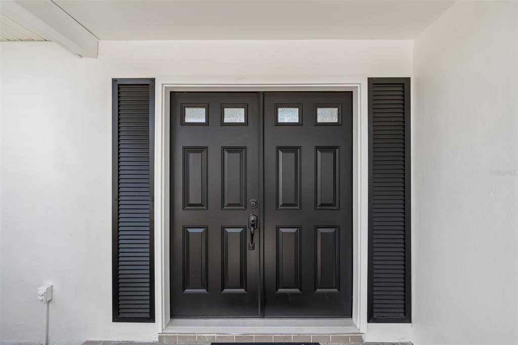 A black double front door with glass panels is flanked by vertical black shutters — 775 CAPRI BOULEVARD, TREASURE ISLAND, FL