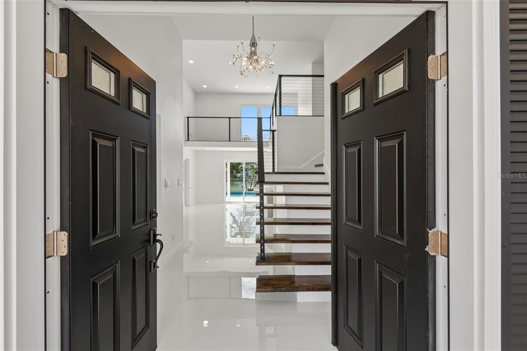 A view through open double doors into a bright foyer with a floating staircase — 775 CAPRI BOULEVARD, TREASURE ISLAND, FL