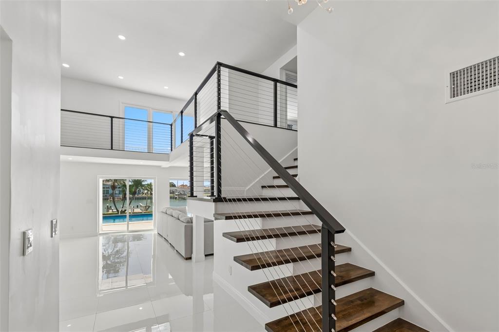 A modern interior features a wooden staircase with cable railings leading to an upper landing — 775 CAPRI BOULEVARD, TREASURE ISLAND, FL