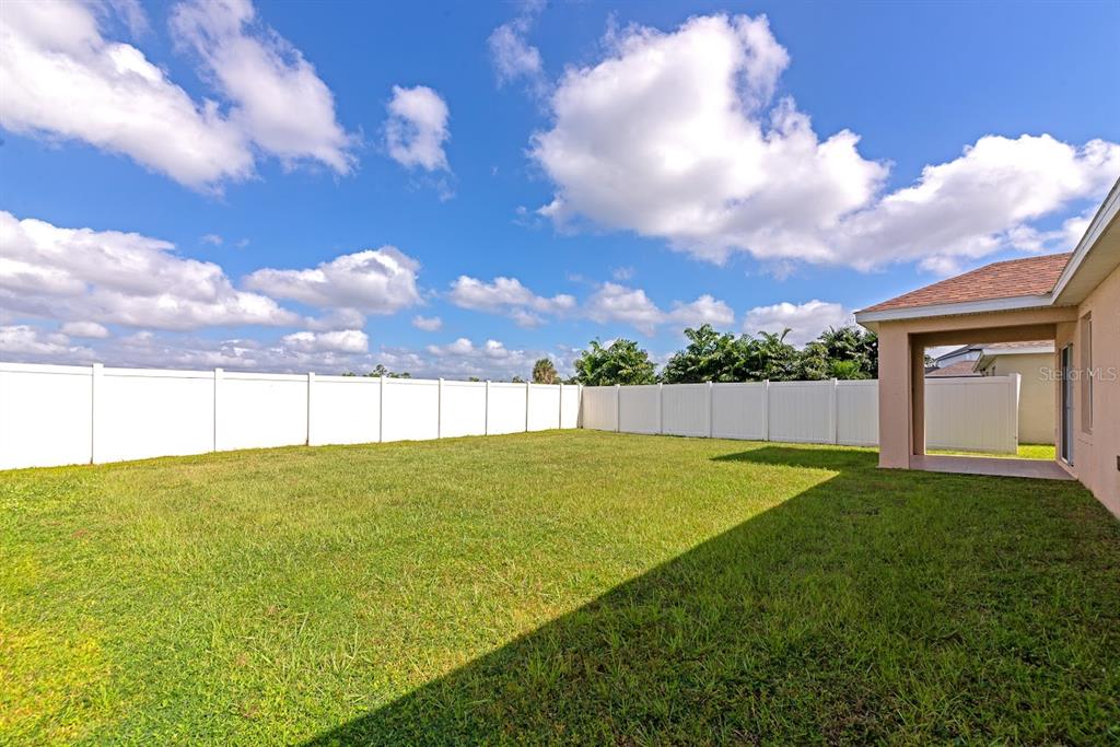 A grassy backyard features a white vinyl privacy fence and a covered patio area — 15517 ROSE GROVE DRIVE, BRADENTON, FL