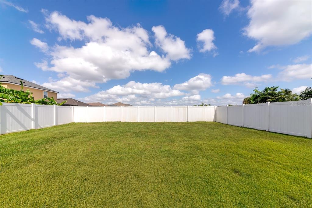 A large, grassy backyard enclosed by a white vinyl privacy fence under a blue sky — 15517 ROSE GROVE DRIVE, BRADENTON, FL