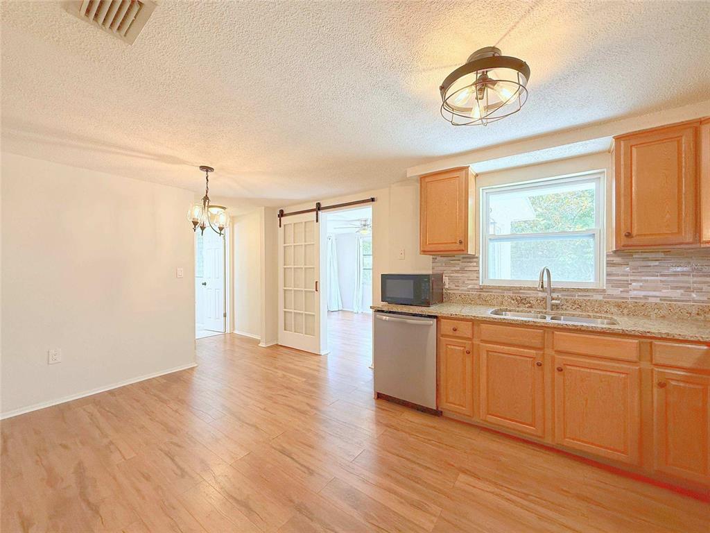 A kitchen with wood cabinets, granite countertops, and light wood flooring opens to a dining area — 15839 VILLA DRIVE, HUDSON, FL
