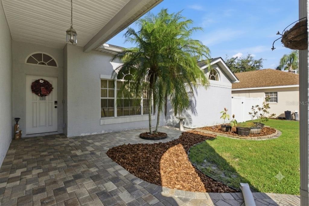 A paved patio leads to a front entrance with a palm tree and landscaped garden — 10050 HERMOSILLO DRIVE, NEW PORT RICHEY, FL