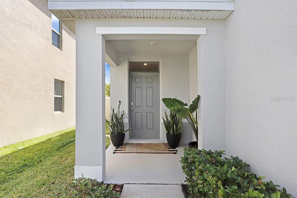 A gray front door is centered under a covered porch with potted plants — 3044 SUNCOAST PLAINS DRIVE, ODESSA, FL
