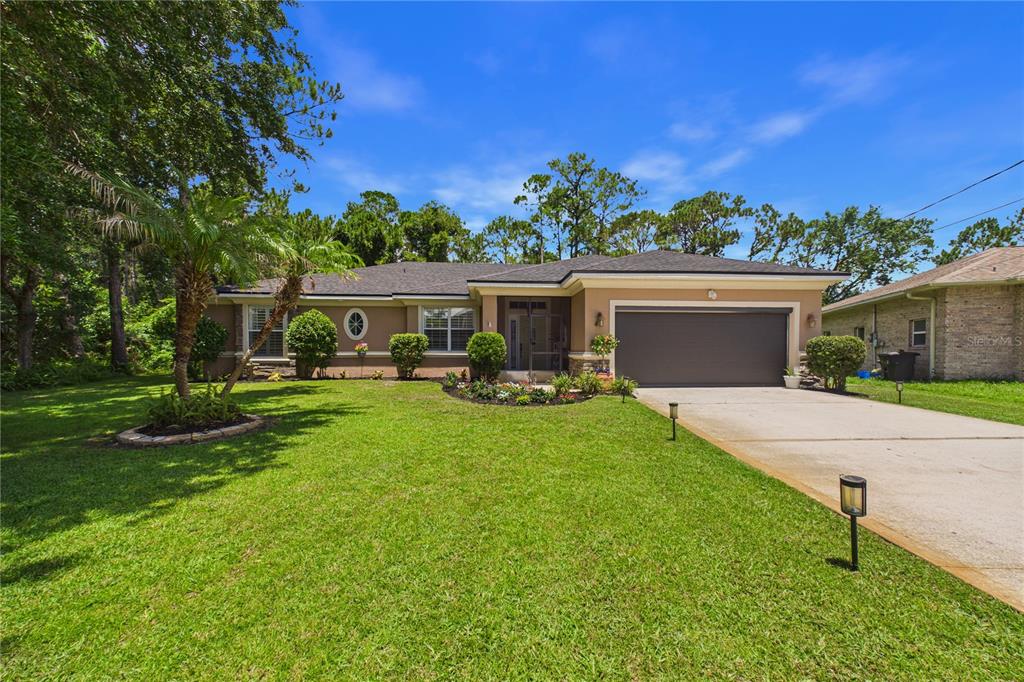 A single-story house with a tan exterior, a two-car garage, and a manicured front lawn — 49 FANSHAWE LANE, PALM COAST, FL
