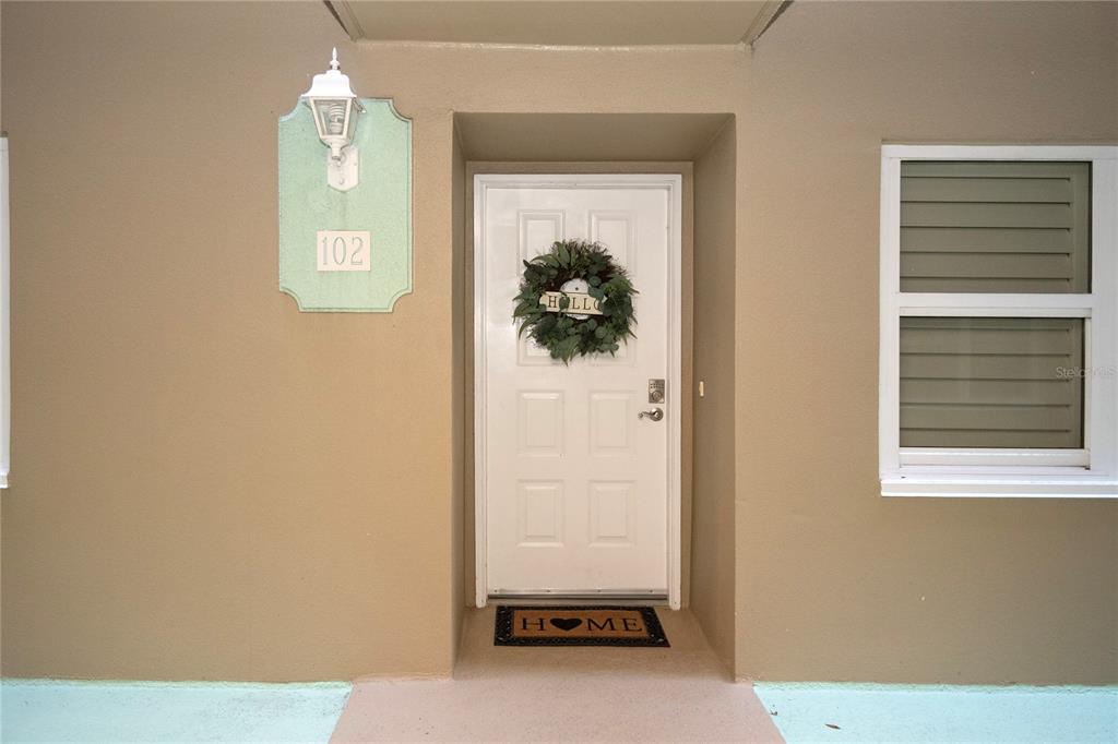 A white front door with a wreath and a welcome mat sits under a light — 4 OCEANS WEST BOULEVARD UNIT 102C, DAYTONA BEACH, FL