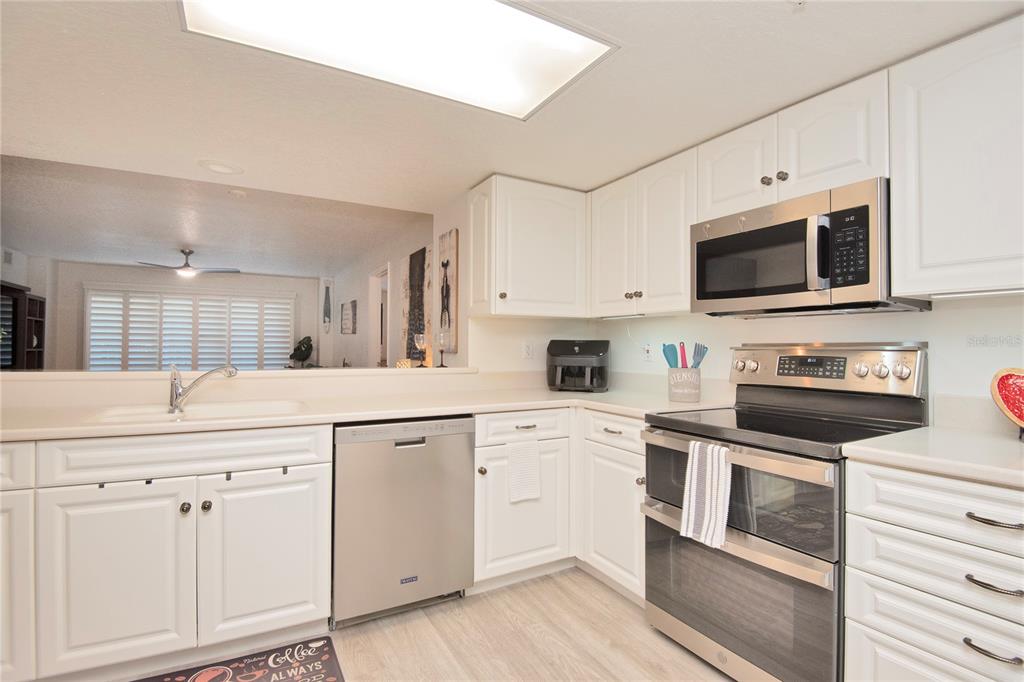 A kitchen features white cabinets, stainless steel appliances, and a pass-through window to the living area — 4 OCEANS WEST BOULEVARD UNIT 102C, DAYTONA BEACH, FL