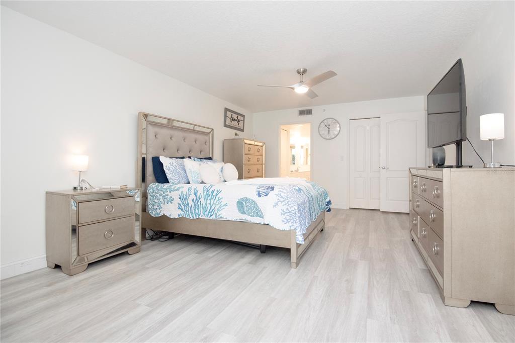 A bedroom features a bed with coral-patterned bedding, mirrored furniture, and light wood-look flooring — 4 OCEANS WEST BOULEVARD UNIT 102C, DAYTONA BEACH, FL
