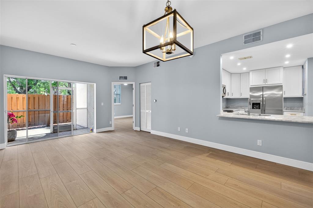 A dining area with wood-look tile floors, a modern chandelier, and a kitchen pass-through window — 4109 BELLASOL CIRCLE UNIT 1113, FORT MYERS, FL