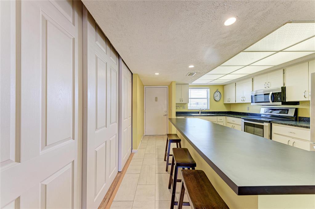 A kitchen features a long breakfast bar, white cabinetry, and light-colored tile flooring — 3983 MACEACHEN BOULEVARD UNIT 434, SARASOTA, FL