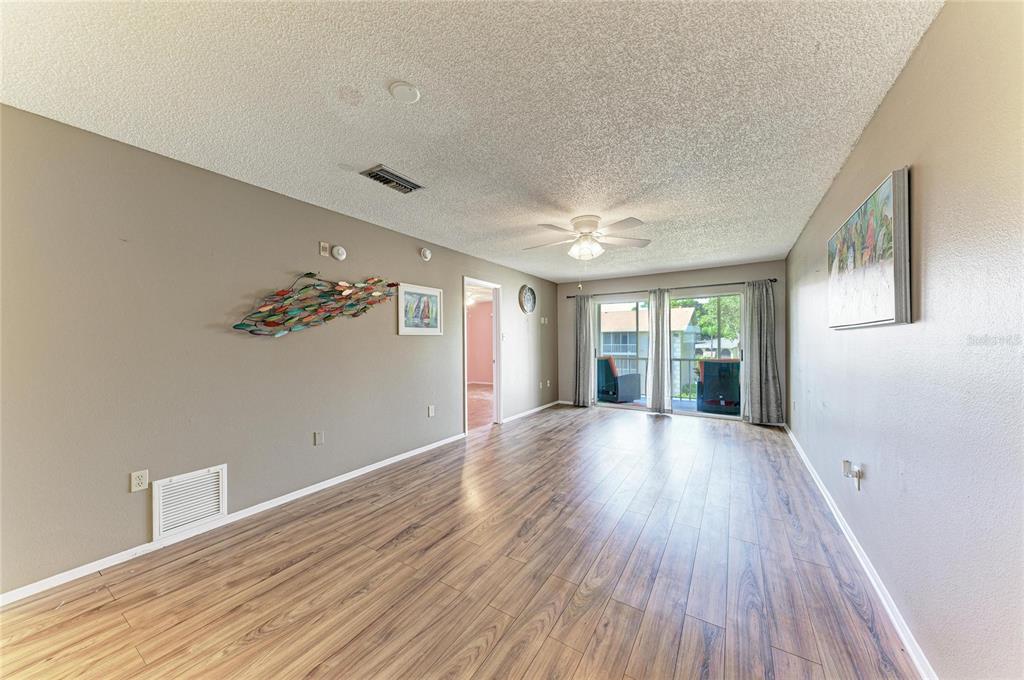 A living room with wood-look flooring, a ceiling fan, and sliding glass doors to a balcony — 3983 MACEACHEN BOULEVARD UNIT 434, SARASOTA, FL