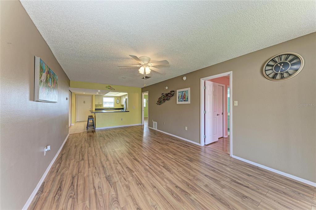 A living room with wood-look flooring, a ceiling fan, and an open kitchen beyond — 3983 MACEACHEN BOULEVARD UNIT 434, SARASOTA, FL