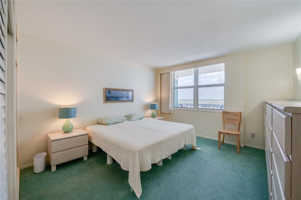 A bedroom features a bed with a white cover, green carpeting, and a large window — 2800 N ATLANTIC AVENUE UNIT 1009, DAYTONA BEACH, FL