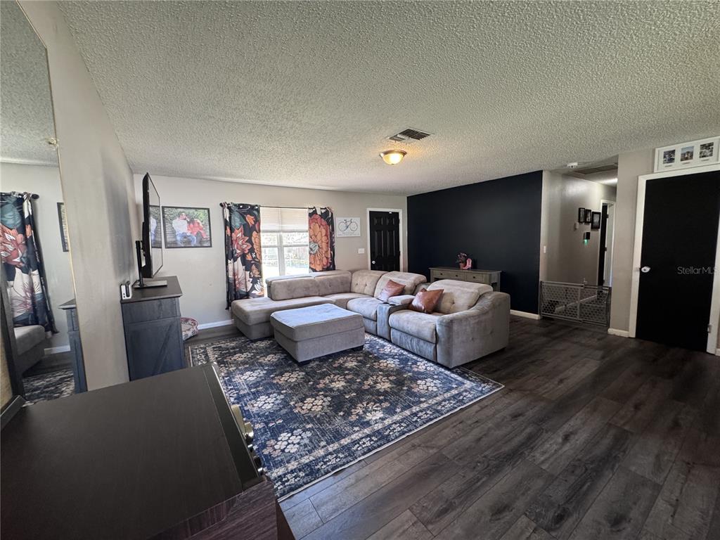 A living room features a sectional sofa, a patterned rug, and a black accent wall — 24 SAPPHIRE WAY, OCALA, FL