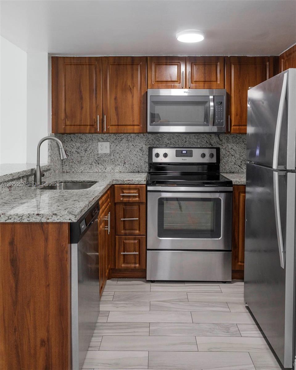 A kitchen features wood cabinets, granite countertops, stainless steel appliances, and light-colored tile flooring — 8580 NW 6th Ln # 205, Miami FL 33126, MIAMI, FL