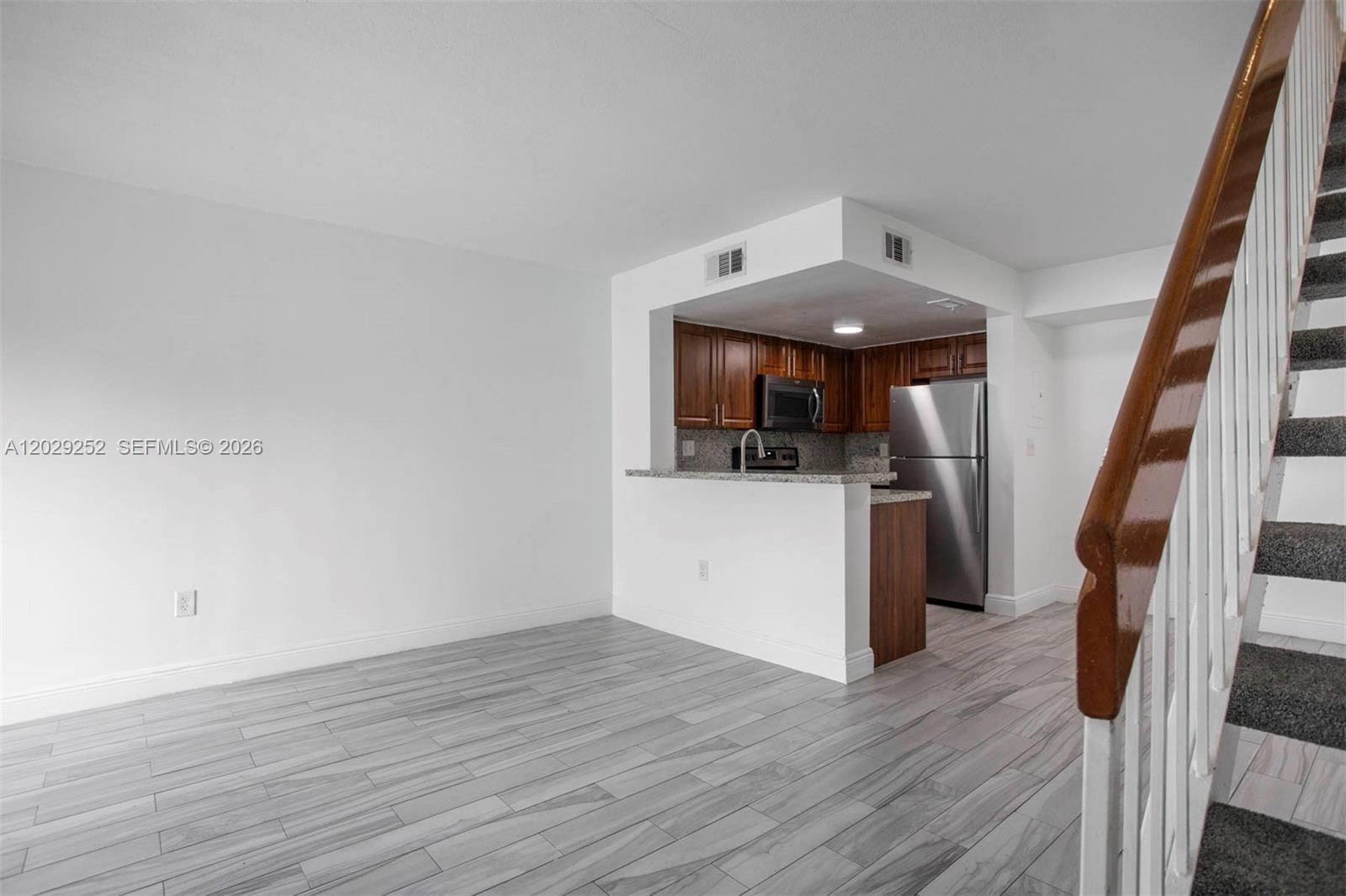 A kitchen with wood cabinets and stainless steel appliances overlooks a room with wood flooring — 8580 NW 6th Ln # 205, Miami FL 33126, MIAMI, FL