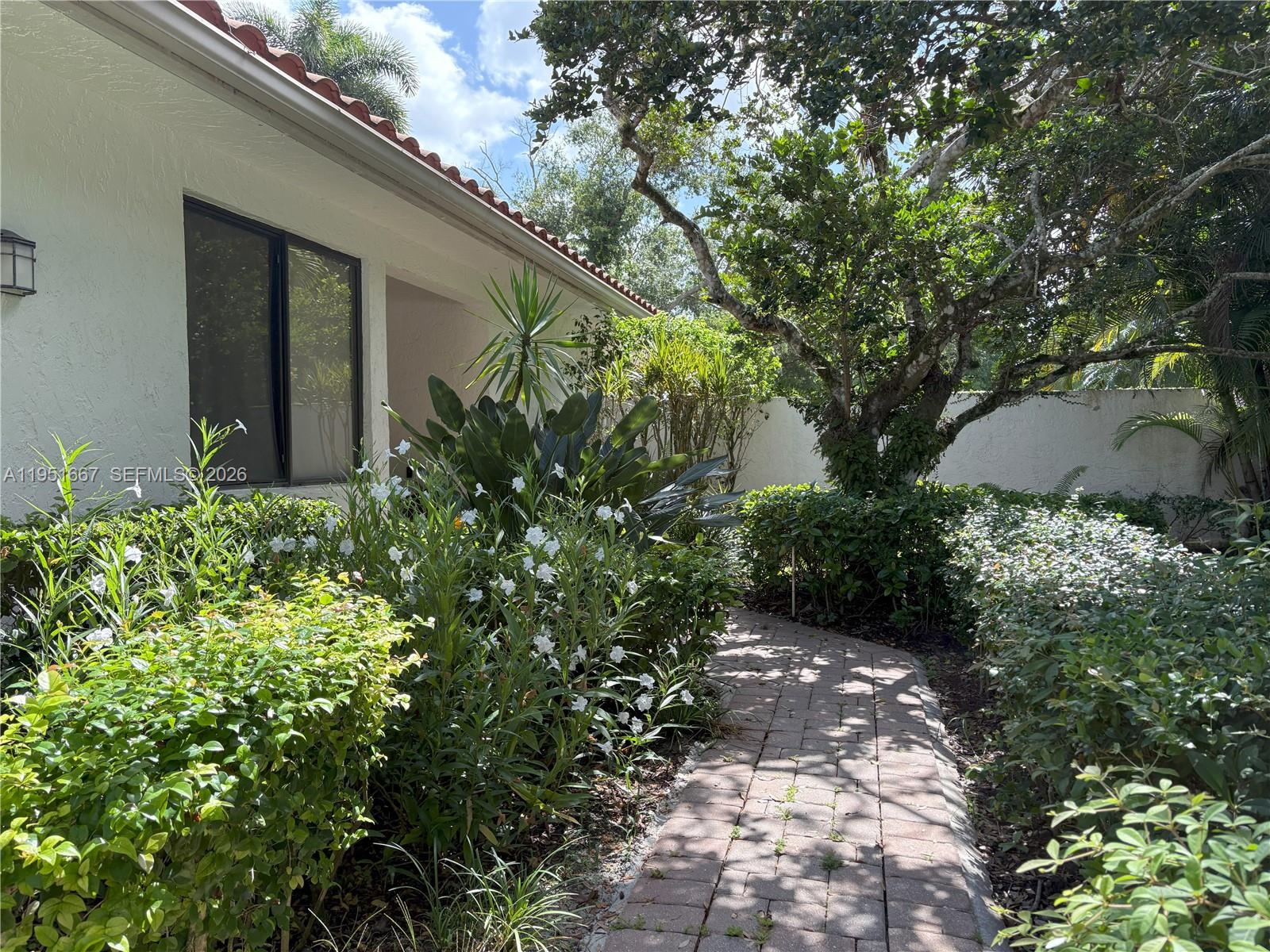 A brick walkway leads to the entrance of a white house surrounded by lush landscaping — 2538 Windsor Way Ct, Wellington FL 33414, WELLINGTON, FL