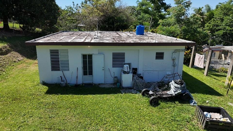 The exterior of a white, single-story house features a flat roof with a blue water tank — CaracolSol SECTOR JUAN MUÑIZ, AGUADA, PR