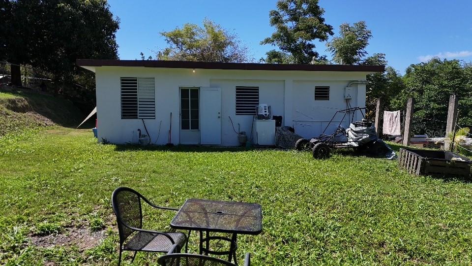 A white, single-story house sits on a grassy lawn with a small table and chairs — CaracolSol SECTOR JUAN MUÑIZ, AGUADA, PR