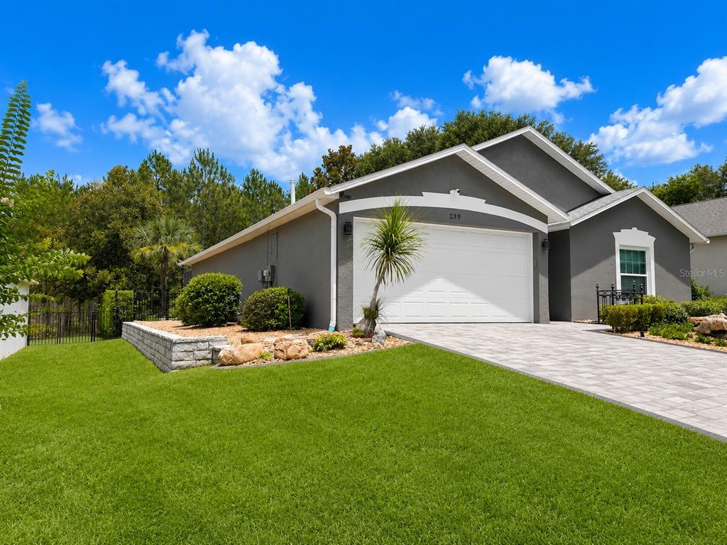 A gray single-story house features a white garage door, paver driveway, and landscaped front yard — 239 CHINA BERRY CIRCLE, DAVENPORT, FL