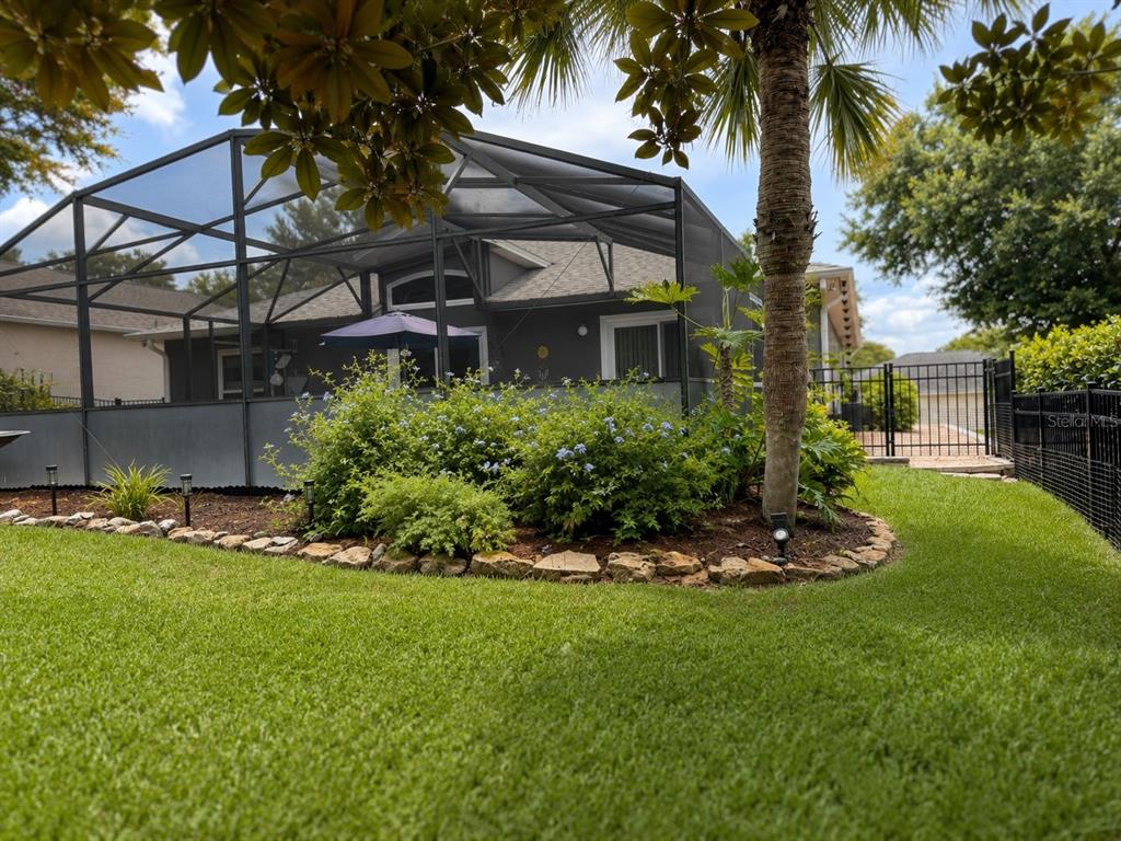 A screened-in pool enclosure sits behind a landscaped garden bed in a grassy backyard — 239 CHINA BERRY CIRCLE, DAVENPORT, FL