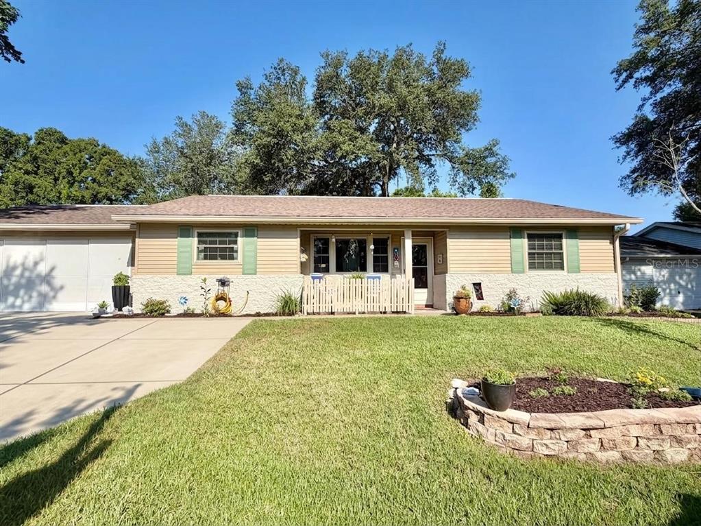 A single-story house with tan siding, stone accents, and a concrete driveway under a clear sky — 10966 SW 85 TERRACE, OCALA, FL