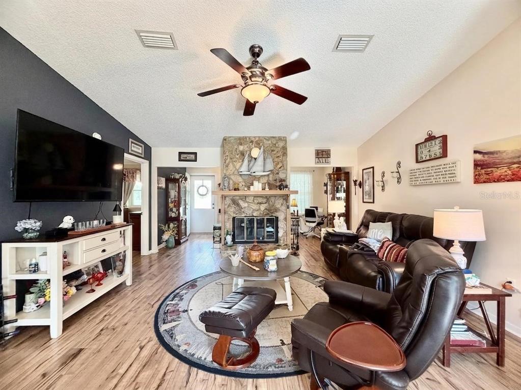 A living room features a stone fireplace, dark wood-look flooring, and a ceiling fan — 10966 SW 85 TERRACE, OCALA, FL