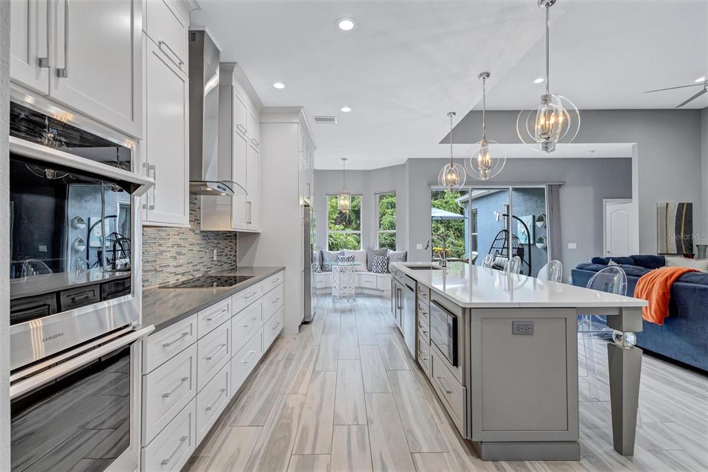 A modern kitchen features white cabinetry, a gray island, stainless steel appliances, and tile flooring — 139 TALL TREES COURT, SARASOTA, FL