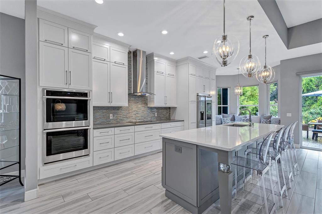 A modern kitchen features white cabinetry, a gray island with bar seating, and stainless appliances — 139 TALL TREES COURT, SARASOTA, FL