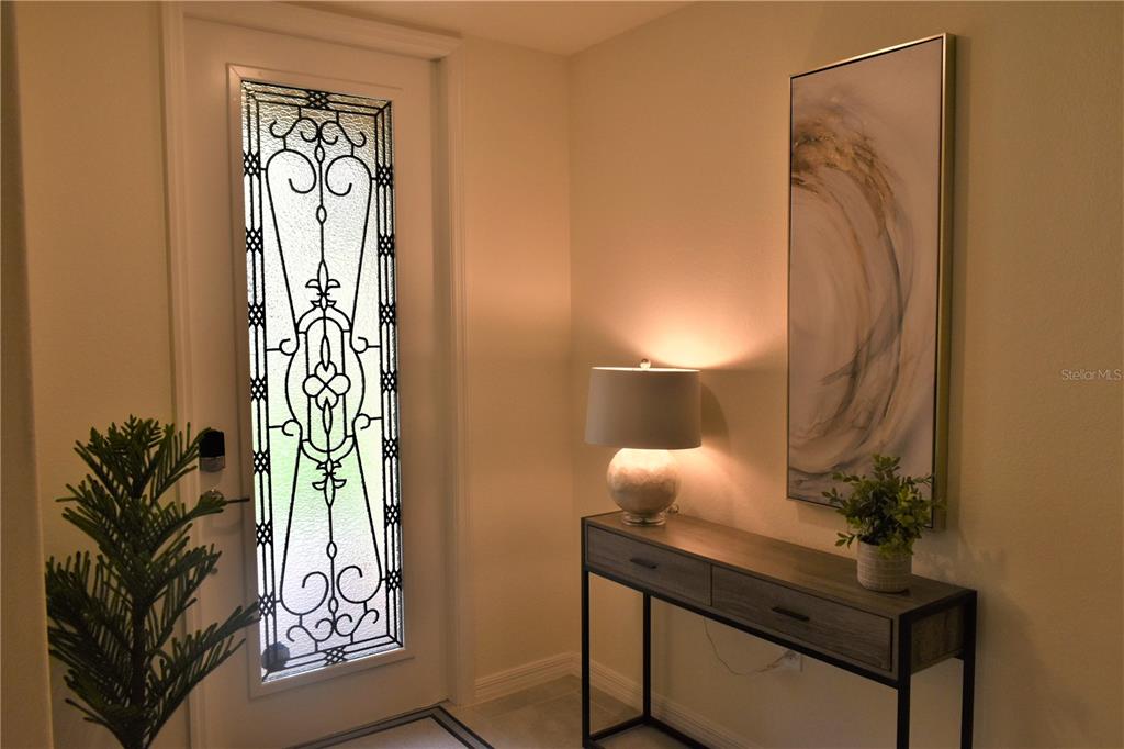 An entryway features a decorative glass-paneled door, a console table with a lamp, and artwork — 12500 GHIBERTI CIRCLE UNIT 102, VENICE, FL
