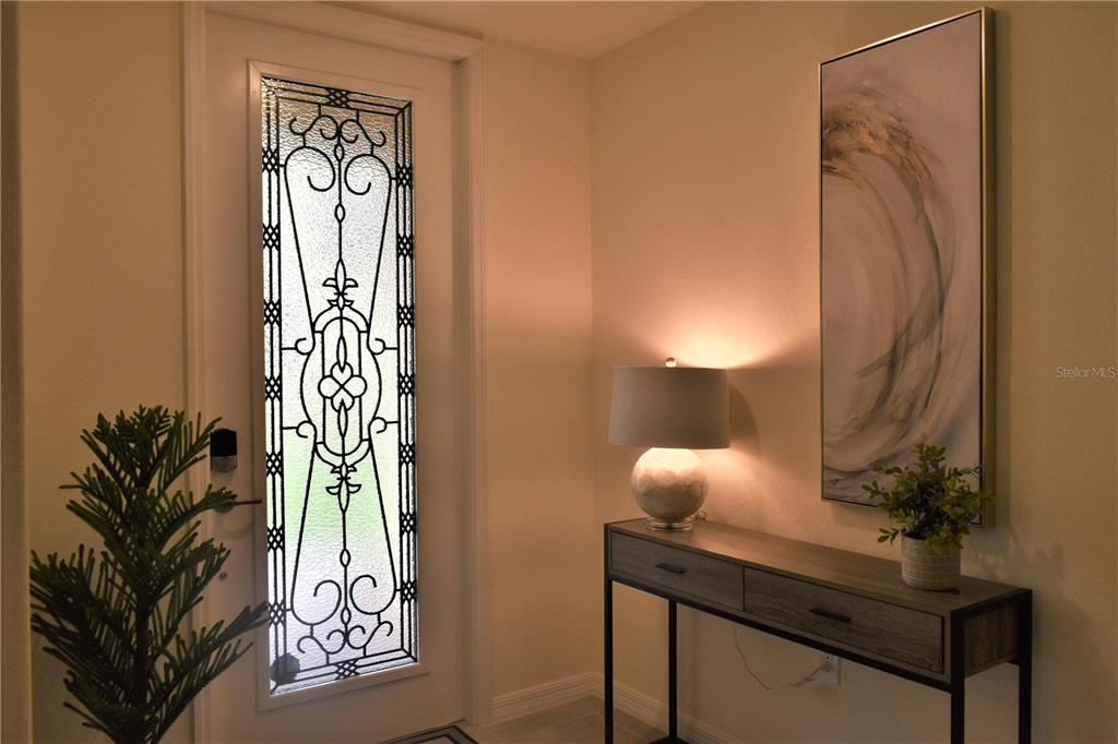 An entryway features a decorative glass-paneled door, a console table with a lamp, and wall art — 12500 GHIBERTI CIRCLE UNIT 102, VENICE, FL