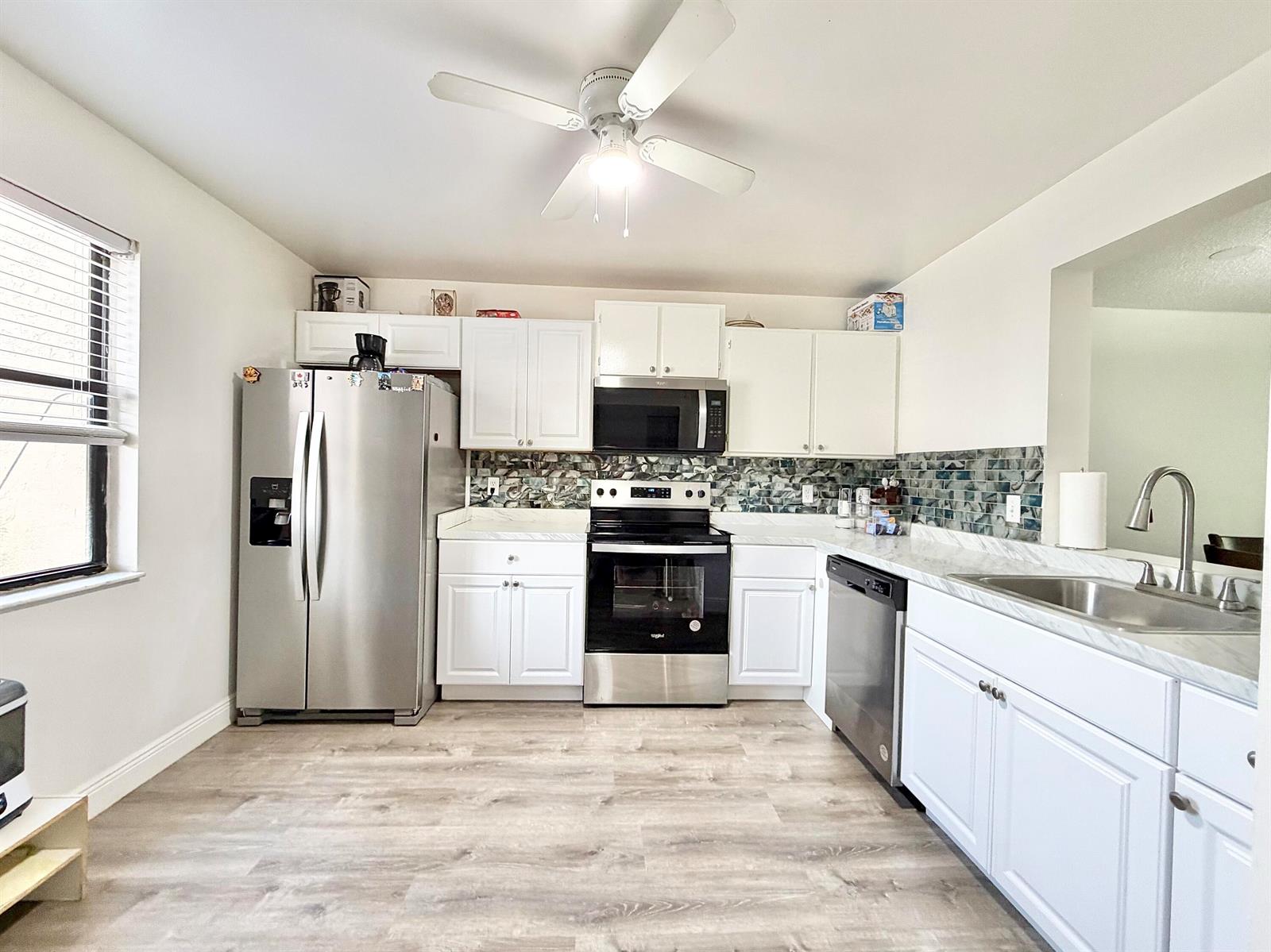 A kitchen features white cabinets, stainless steel appliances, a patterned backsplash, and light wood flooring — 1407 E Lakeview Dr Drive E, Royal Palm Beach FL 33411, ROYAL PALM BEACH, FL