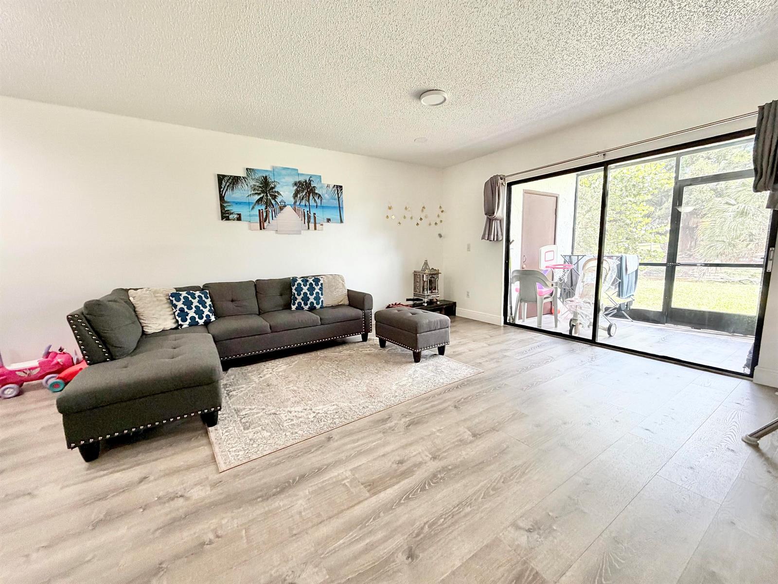 A living room features gray sectional seating, a patterned rug, and a sliding glass door — 1407 E Lakeview Dr Drive E, Royal Palm Beach FL 33411, ROYAL PALM BEACH, FL