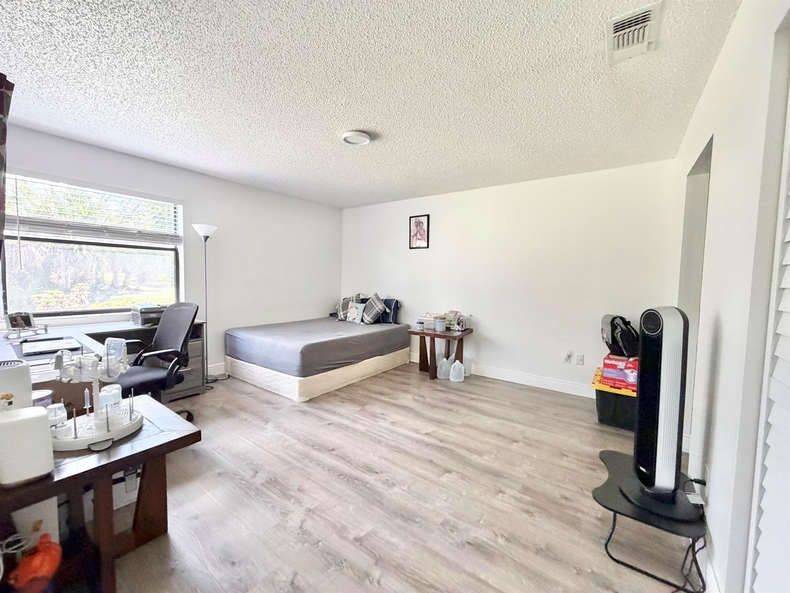A bedroom features light wood-look flooring, a bed, a desk, and a window — 1407 E Lakeview Dr Drive E, Royal Palm Beach FL 33411, ROYAL PALM BEACH, FL