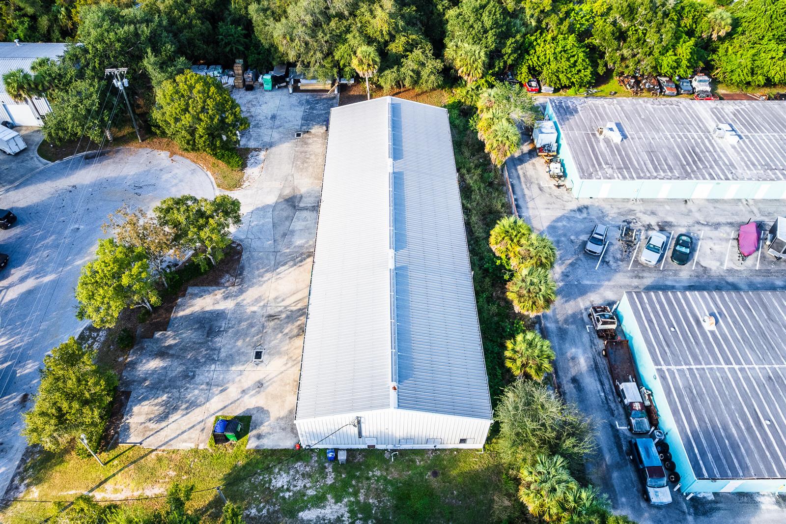 An aerial view shows a long, rectangular metal warehouse building surrounded by trees and pavement — 820 35th Court SW, Vero Beach FL 32968, VERO BEACH, FL