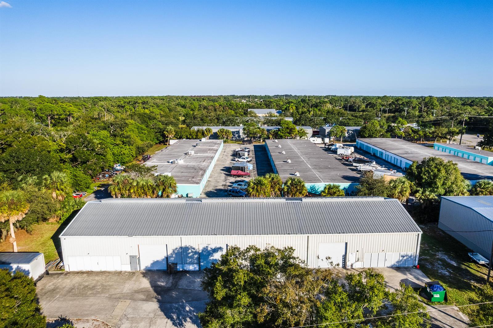 An aerial view shows several industrial warehouse buildings with metal roofs surrounded by trees — 820 35th Court SW, Vero Beach FL 32968, VERO BEACH, FL