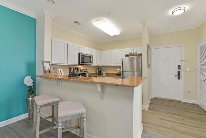 A kitchen with white cabinets, granite countertops, and a breakfast bar next to an entryway — 1301 TUSCAN TERRACE UNIT 9407, DAVENPORT, FL