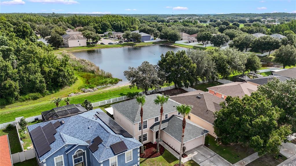 An aerial view shows several suburban houses with tiled roofs situated near a small lake — 17017 TORVEST COURT, LAND O LAKES, FL