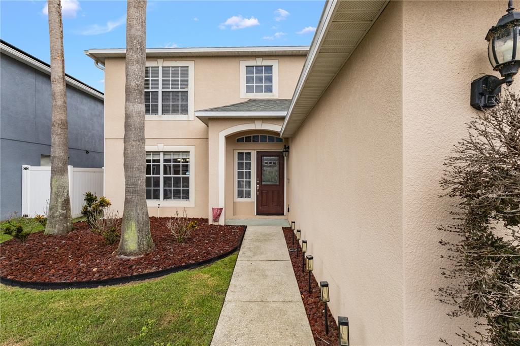 A two-story beige house with a front walkway, palm trees, and a brown front door — 17017 TORVEST COURT, LAND O LAKES, FL