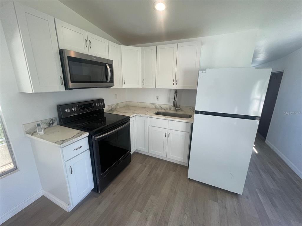 A kitchen features white cabinets, stainless steel appliances, a white refrigerator, and light wood flooring — 7489 CHARLIN PARKWAY, ORLANDO, FL