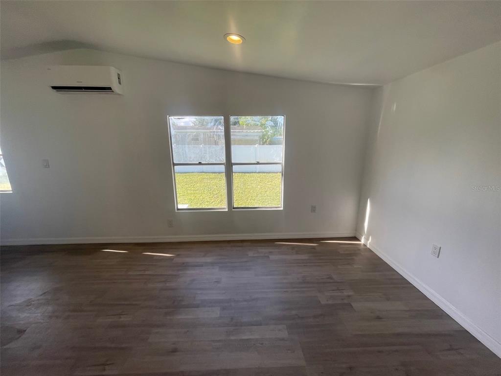 An empty room with white walls, wood-look flooring, a mini-split unit, and two windows — 7489 CHARLIN PARKWAY, ORLANDO, FL