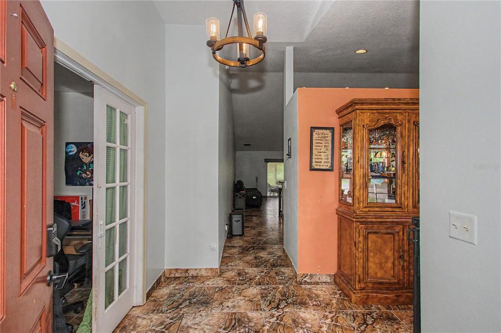 An entryway with tiled floors, a wooden hutch, and a chandelier leads into a living area — 8137 SW 138TH STREET ROAD, OCALA, FL