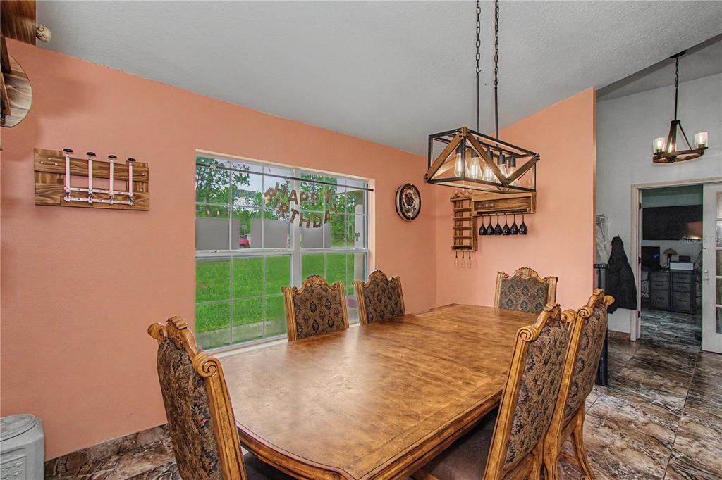 A dining room features a wooden table, patterned chairs, peach walls, and a rectangular pendant light — 8137 SW 138TH STREET ROAD, OCALA, FL
