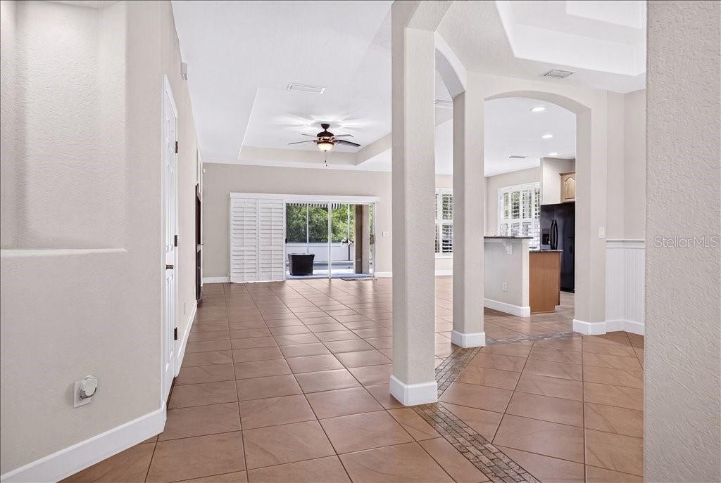 An open-concept living area with tile flooring, a tray ceiling, and a view of the patio — 63 WESTLAND RUN, ORMOND BEACH, FL