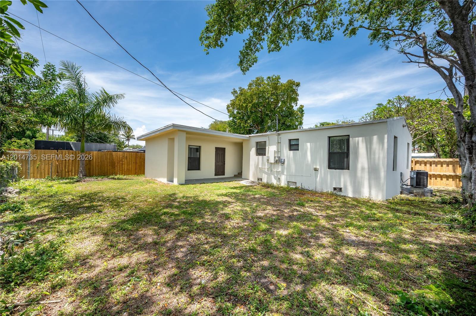 The exterior of a single-story house features a white stucco facade and a grassy backyard — 2106 Plunkett Ct, Hollywood FL 33020, HOLLYWOOD, FL