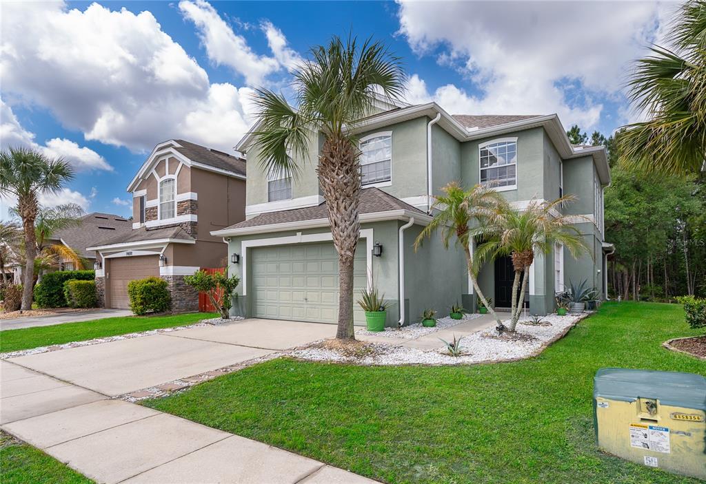 A two-story green house with a two-car garage and a palm tree in the front — 14697 HUNTCLIFF PARK WAY, ORLANDO, FL