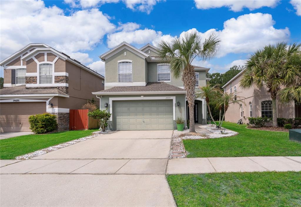 A two-story suburban house with a light green exterior, a two-car garage, and palm trees — 14697 HUNTCLIFF PARK WAY, ORLANDO, FL